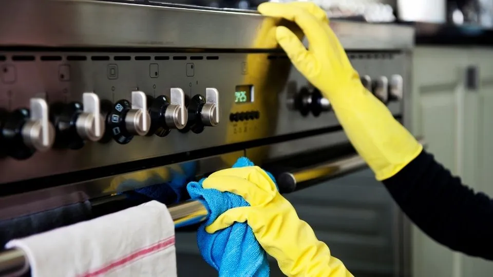 A cleaner in yellow gloves wiping down the front of a stainless steel oven